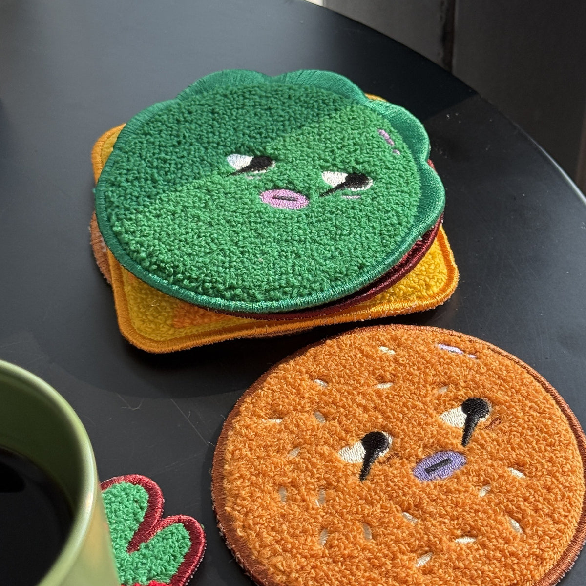 Daging Burger Coaster Stack — lettuce coaster on a stack with the top bun in front, on a dark table